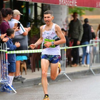 Ludovic Delpuech en course sur route sous la pluie devant une brasserie